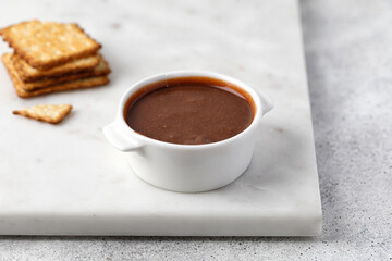 Liquid Chocolate paste in a white sauce pan on a marble tray. Cookies on background