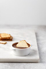 Crackers or cookies in chocolate paste in white sauce pan on marble background.