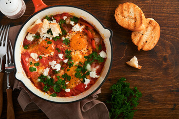 Shakshuka. Homemade fried eggs poached in sauce of tomatoes, olive oil, peppers, onion and garlic in iron frying pan on old wooden background. Traditional cuisine of Israel. Late breakfast concept.