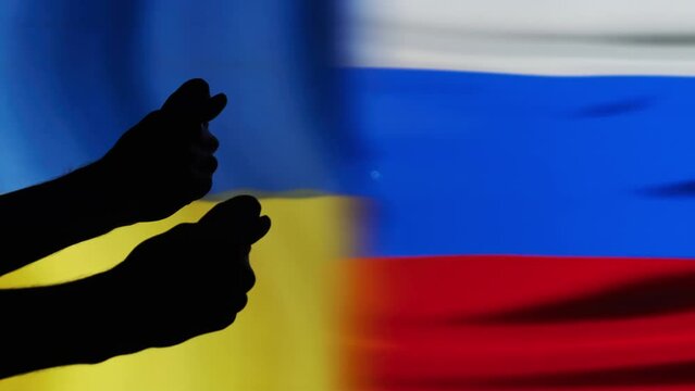 The gesture of the middle finger towards Russia on the background of the flags Ukraine and Russia. Silhouette of male hand meaning sign Fuck you or fuck off Russia. Stop war. Russia started the war.