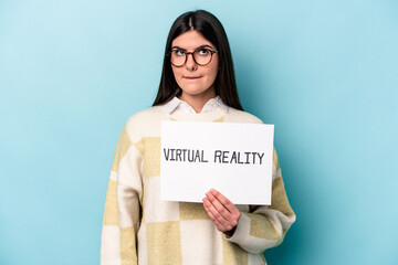 Young caucasian woman holding a virtual reality placard isolated on blue background confused, feels...