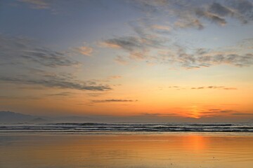 Sunset on the beach, with tropical weather. Sky reddened calm waves in the sea, few clouds in the sky. Bertioga, Itaguare beach, Brazil