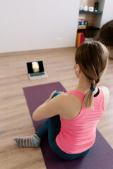 Back view authentic woman practicing yoga at home using online training instructions