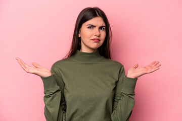 Young caucasian woman isolated on pink background doubting and shrugging shoulders in questioning gesture.