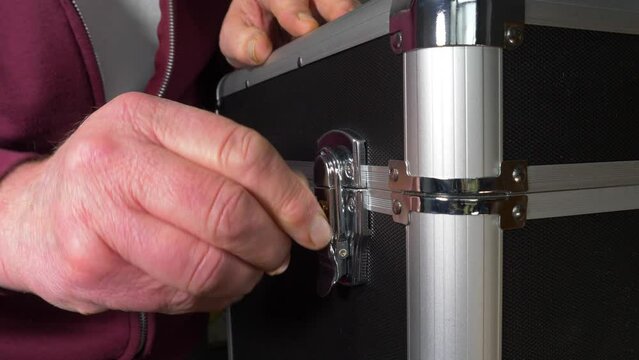 Closeup of a man&rsquo;s hands securing one of the two latches on the lid of a protective storage case / flight case, then using a key to lock it.