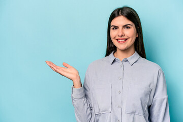 Young caucasian woman isolated on blue background showing a copy space on a palm and holding...