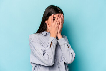 Young caucasian woman isolated on blue background blink through fingers frightened and nervous.