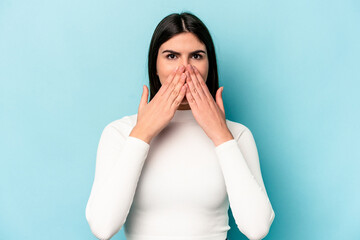 Young caucasian woman isolated on blue background shocked covering mouth with hands.