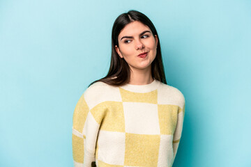 Young caucasian woman isolated on blue background shrugs shoulders and open eyes confused.