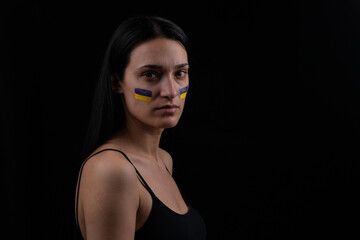 Fototapeta na wymiar Portrait of serious ukrainian woman with blue and yellow ukrainian flag on her cheek.The symbol of the inviolability of the Ukrainian people. Dark background. Space for your text