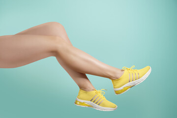 Studio shot of a young woman's legs in a pair of yellow sport shoes for running on turquoise...