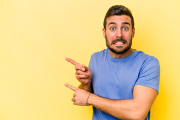 Young caucasian man isolated on yellow background shocked pointing with index fingers to a copy space.