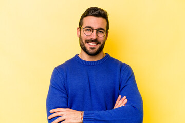 Young caucasian man isolated on yellow background who feels confident, crossing arms with determination.