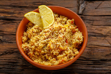Couscous masfouf with dried fruits and nuts in a clay plate on a wooden table.