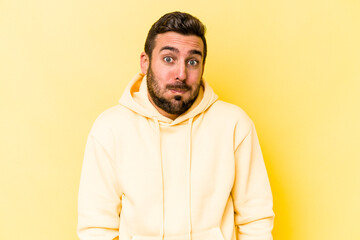 Young caucasian man isolated on yellow background shrugs shoulders and open eyes confused.