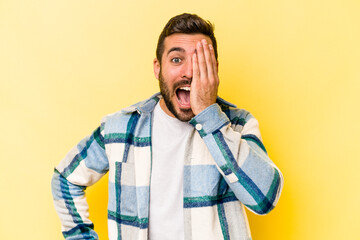 Young caucasian man isolated on yellow background having fun covering half of face with palm.