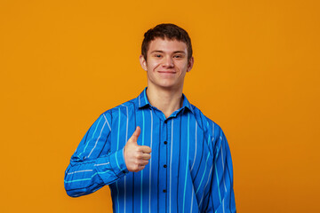 Portrait of a positive young man, smiling and showing a raised thumb, as a sign of approval. A young man, emotionally excited, looks into the camera, standing on a yellow background in the studio