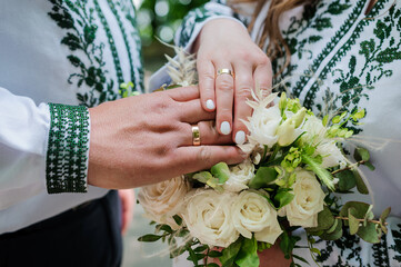 Hands of newlyweds with golden rings on a bouquet of flowers. Hands of the bride and groom on a beautiful bouquet