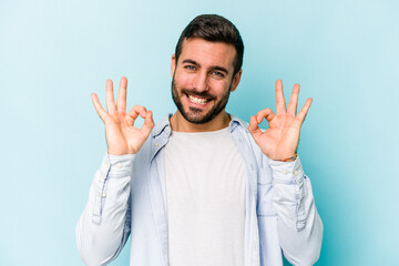 Young caucasian man isolated on blue background cheerful and confident showing ok gesture.