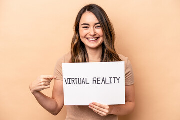 Fototapeta na wymiar Young caucasian woman holding a virtual reality placard isolated on beige background smiling and pointing aside, showing something at blank space.