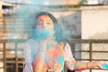 Pretty Young indian smart girl with face coloured with gulal for festival of colours Holi blowing...