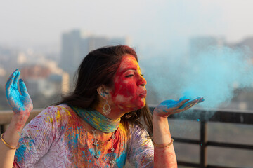 Pretty Young indian smart girl with face coloured with gulal for festival of colours Holi blowing...