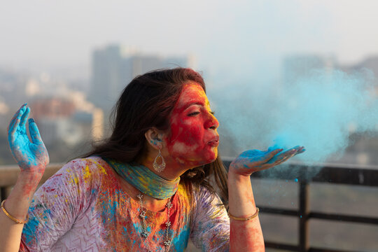 Pretty Young indian smart girl with face coloured with gulal for festival of colours Holi blowing holi color powder, a popular hindu festival celebrated across india