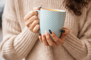A girl in a beige sweater with a blue mug in her hands. Blue porcelain mug mockup for your design