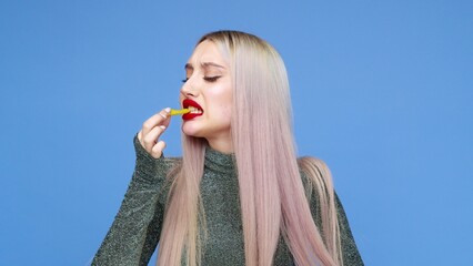 Close-up of a girl paints her lips with red lipstick and starts eating a hamburger with pleasure on a blue background. Diet. The concept of healthy and unhealthy food. fast food