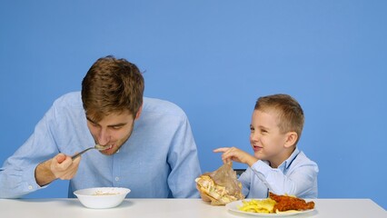 A man and a boy are sitting at the table, the man is eating porridge, and the boy is eating fast food. The concept of healthy and unhealthy food. Fast food