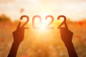 2022 is supported by hands on the background of a sunny sunset.