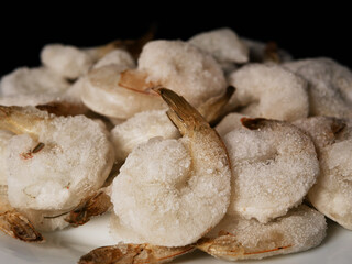 Frozen king prawns on a white plate, black background