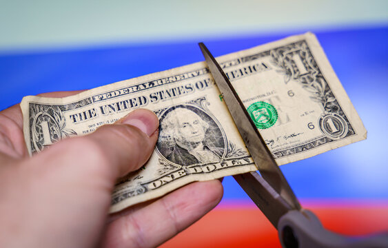 hand with scissors cutting a dollar bill with the russian flag in the background.