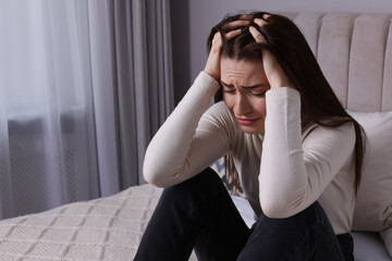 Sad young woman crying on bed at home, space for text. Loneliness concept