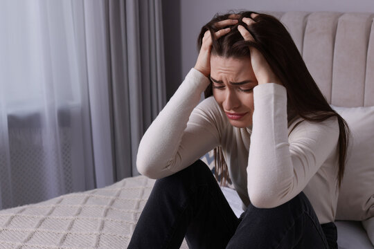 Sad young woman crying on bed at home, space for text. Loneliness concept