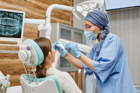 Waist up portrait of young female dentist examining patient sitting in chair at dental clinic