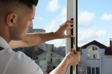Man putting rubber draught strip onto window indoors, focus on hands - obrazy, fototapety, plakaty