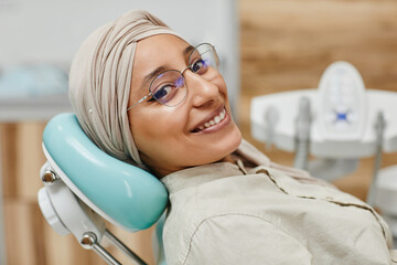Close up portrait of young Middle-Eastern woman lying in dental chair and smiling at camera