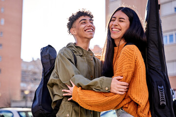 Portrait of a beautiful young couple laughing outdoors with guitar handbag, the friends are hugging...