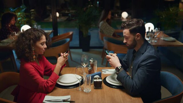 Multiethnic partners searching phone device on fancy restaurant dinner date. 