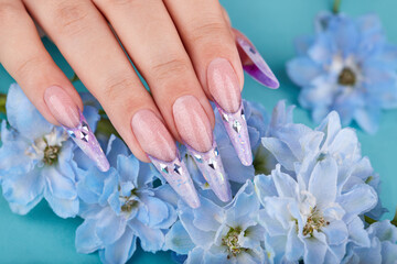 Fototapeta premium Hand with long artificial french manicured nails decorated with gemstones and blue flowers. Fashion and stylish manicure.