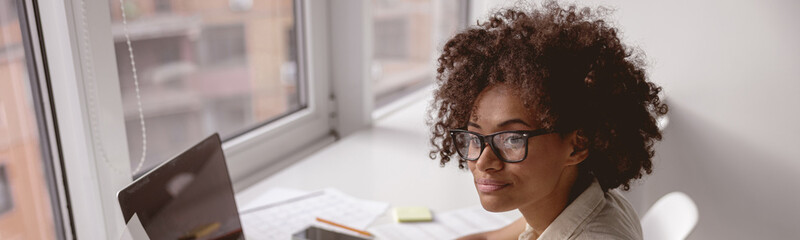 Portrait of cheerful business African-American woman working on laptop