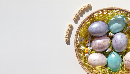 Easter concept. Pink, purple and blue eggs in a wicker basket with straw on a white background. Minimalism.