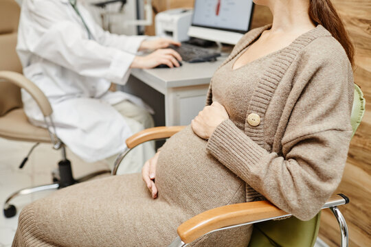 Cropped Shot Of Pregnant Young Woman Consulting Obgyn In Medical Clinic With Focus On Belly, Copy Space