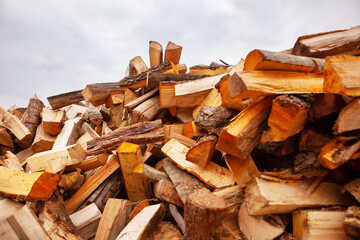 A pile of split firewood for heating a house, in an open space, close-up, against a blue cloudy sky.