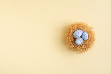 Three blue pastel Easter eggs in nest on a sunny yellow background. Minimal creative concept of Easter.