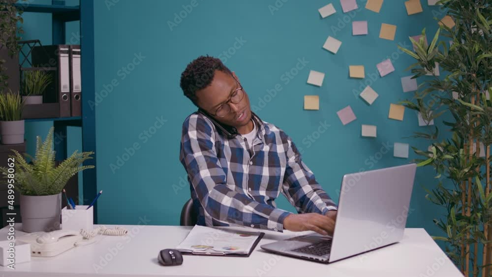 Poster business man using smartphone to talk on phone call while he works on laptop to create financial str