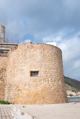 Fototapeta na wymiar In Castellamare di golfo, in Sicily, stands an old castle from the 14th century on the coast. Part of the fort can be seen in portrait format against a blue sky.
