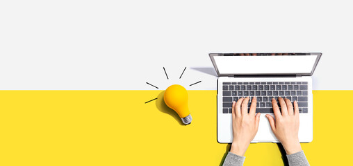 Person using a laptop computer and a light bulb - Flat lay