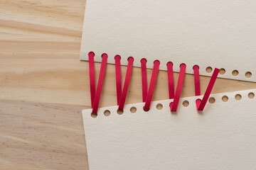 paper with holes and red strips of paper on a wooden surface
